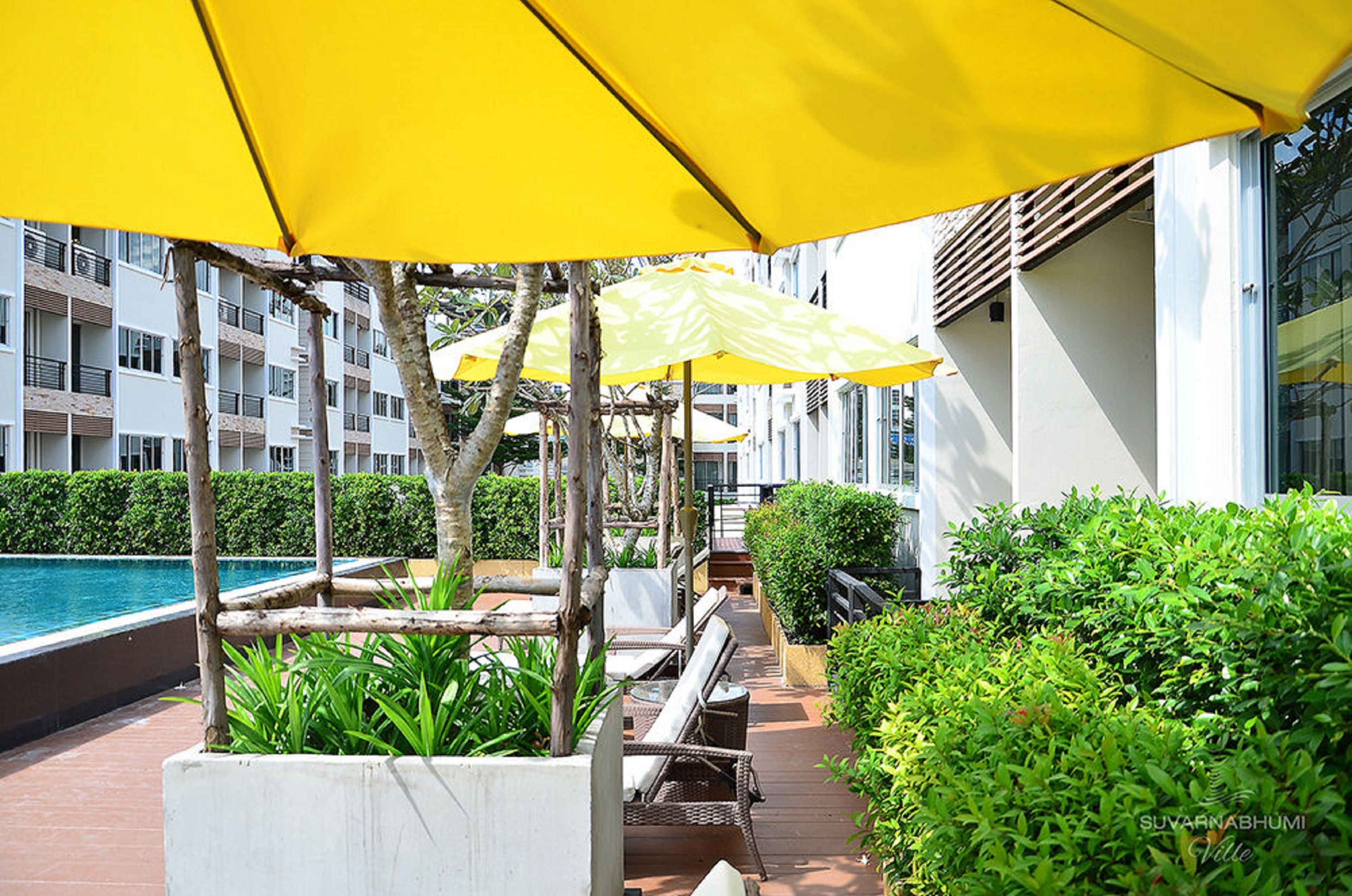 A rooftop terrace with yellow umbrellas, outdoor seating, and a pool in the background.