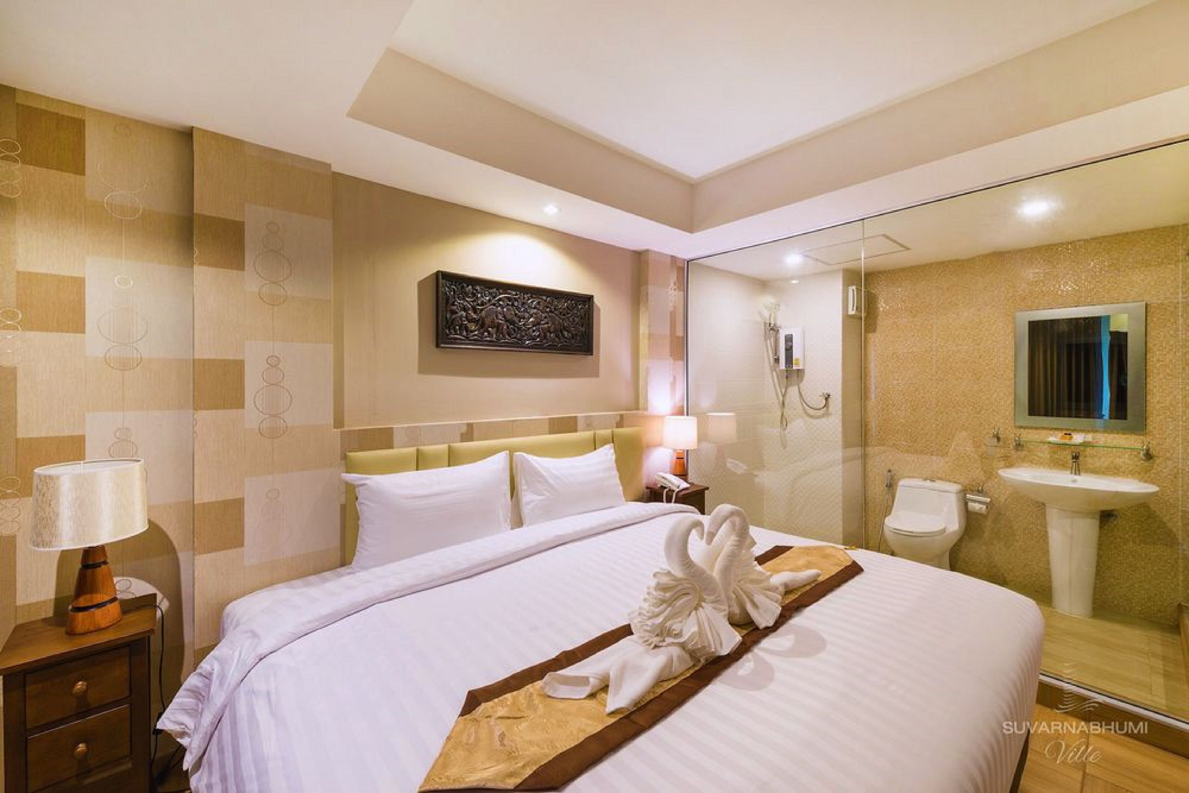 A hotel room with a large bed, a bedside table with a lamp, a wall-mounted artwork, a glass shower enclosure, and a bathroom with a sink and toilet.