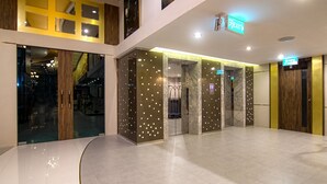 A spacious lobby with a curved floor, glass doors, and a marble elevator. - Gallery Design Hotel (Sisaket)