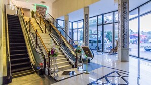 A spacious lobby with a grand staircase, large windows, and decorative columns. - Gallery Design Hotel (Sisaket)