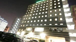 En byggnad med flera våningar och många fönster, en parkeringsplats med flera bilar och en grön lampa högst upp.