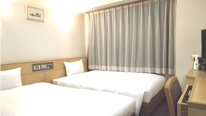 Ett hotellrum med två sängar, ett skrivbord, en stol, en tv och ett fönster med gardiner.