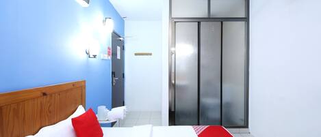 Habitación de hotel con cabecera de madera, cama con ropa de cama blanca y roja, corredor a rayas rojas y blancas, baño con lavamanos y toalla blancos, y puerta corredera a la derecha.