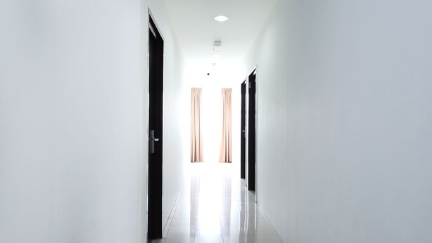 A long, narrow hallway with white walls and a tiled floor, leading to a room with a window and curtains. - Hotel O Midah Inn Puchong (Seri Kembangan)