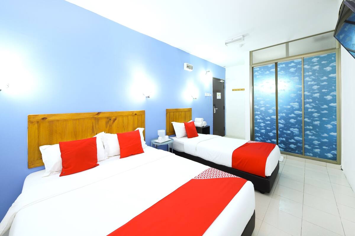 A hotel room with two beds, a window with a view of the sky, and a door to the bathroom.