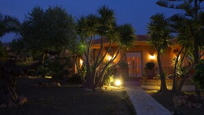 A well-lit residential property at dusk with a paved pathway leading to the entrance, surrounded by palm trees and a landscaped garden. - Villa Concordia (Agrigento)