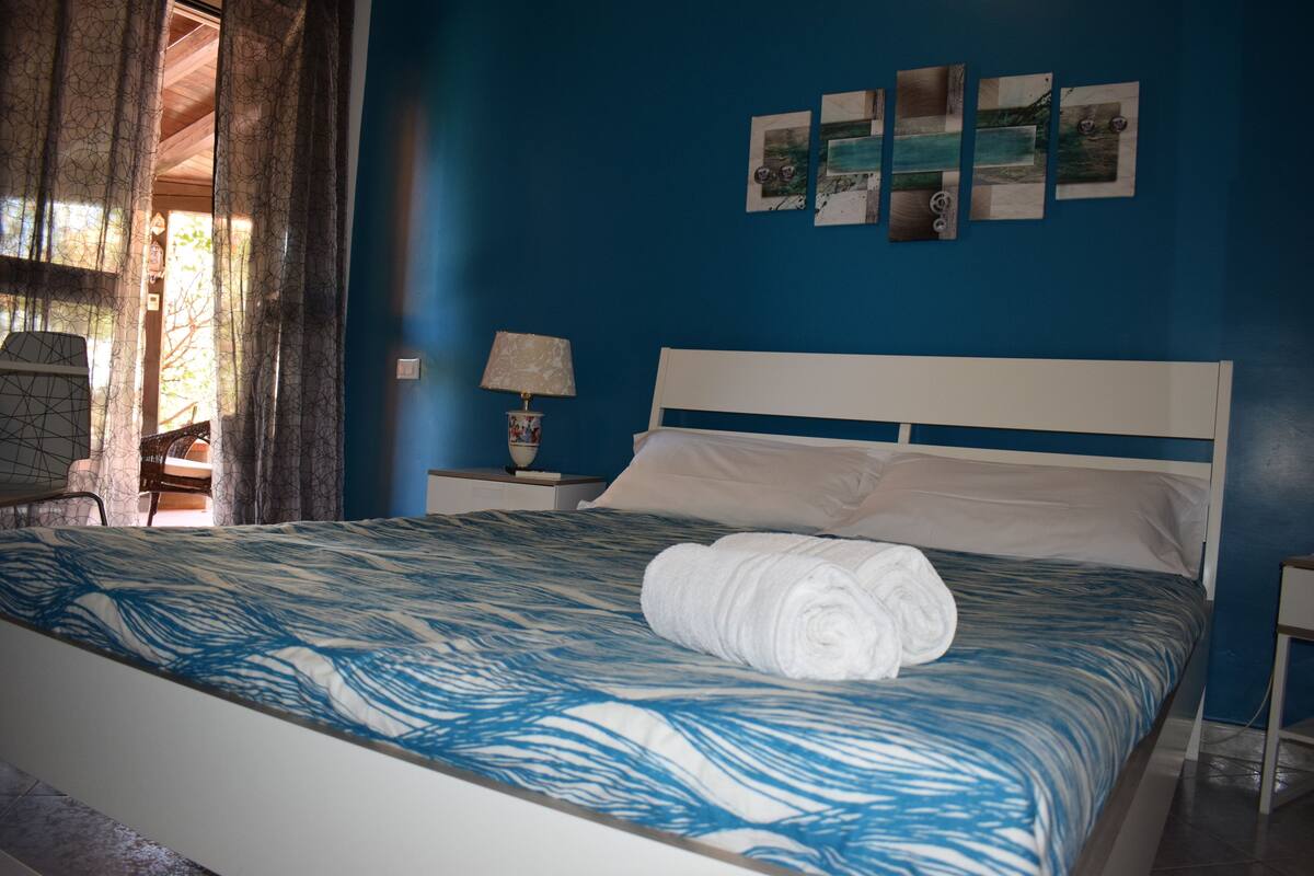 Un dormitorio con cama, mesita de noche, lámpara y ventana con cortinas.
