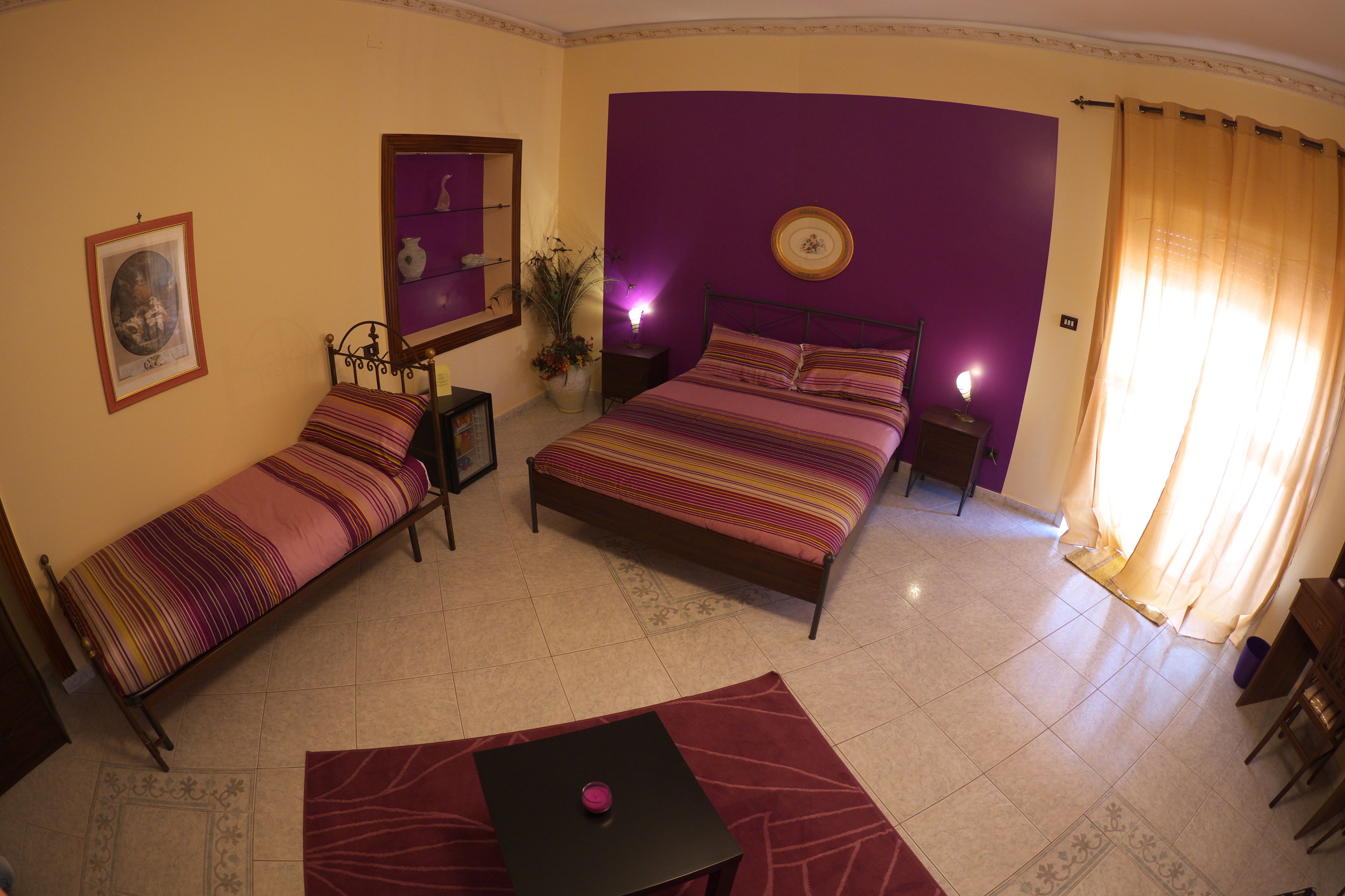 A bedroom with two single beds, a nightstand, a bedside table, a lamp, a mirror, and a window with curtains.