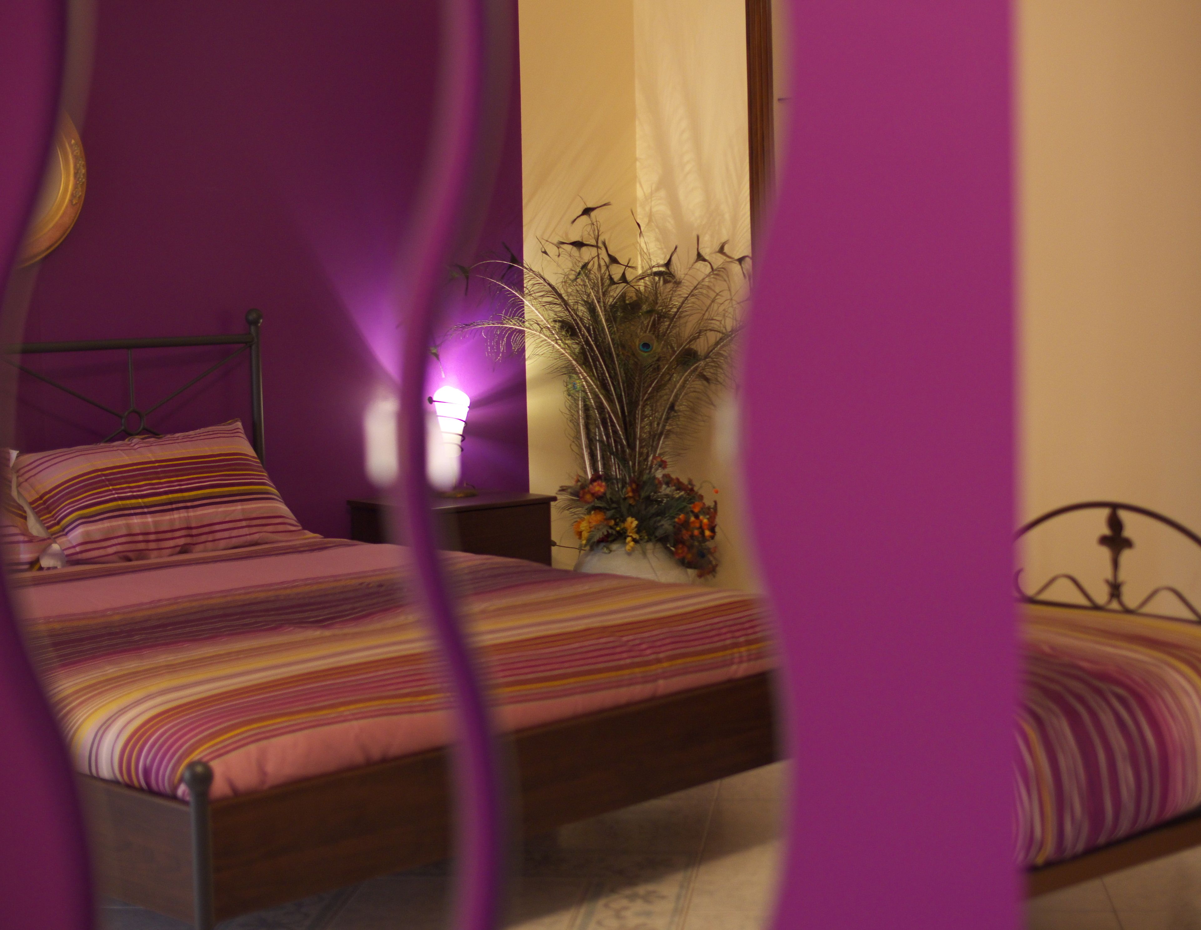 Een slaapkamer met een bed, nachtkastje, lamp en een vaas met bloemen.