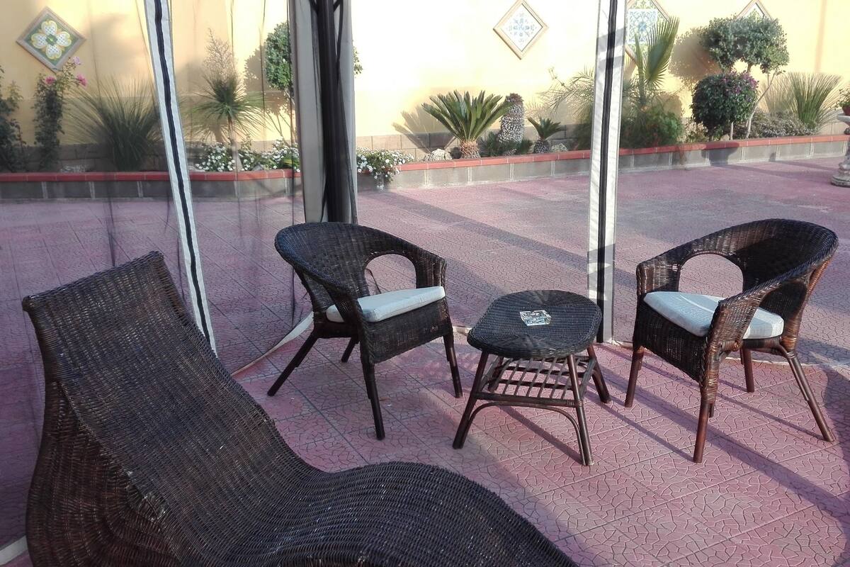 Un patio con mobiliario de mimbre, incluyendo dos sillones y una mesita, y un sofá.