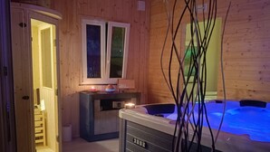 A wooden cabin interior with a hot tub, a small kitchen area, and a door leading to a wooden deck. - Villa Concordia (Agrigento)