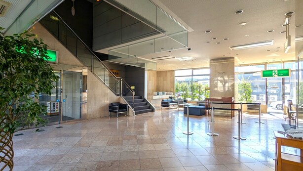 A spacious lobby with a modern staircase, seating areas, and large windows offering views of the outside.