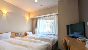 A hotel room with two beds, a desk with a TV and phone, and a window with curtains.