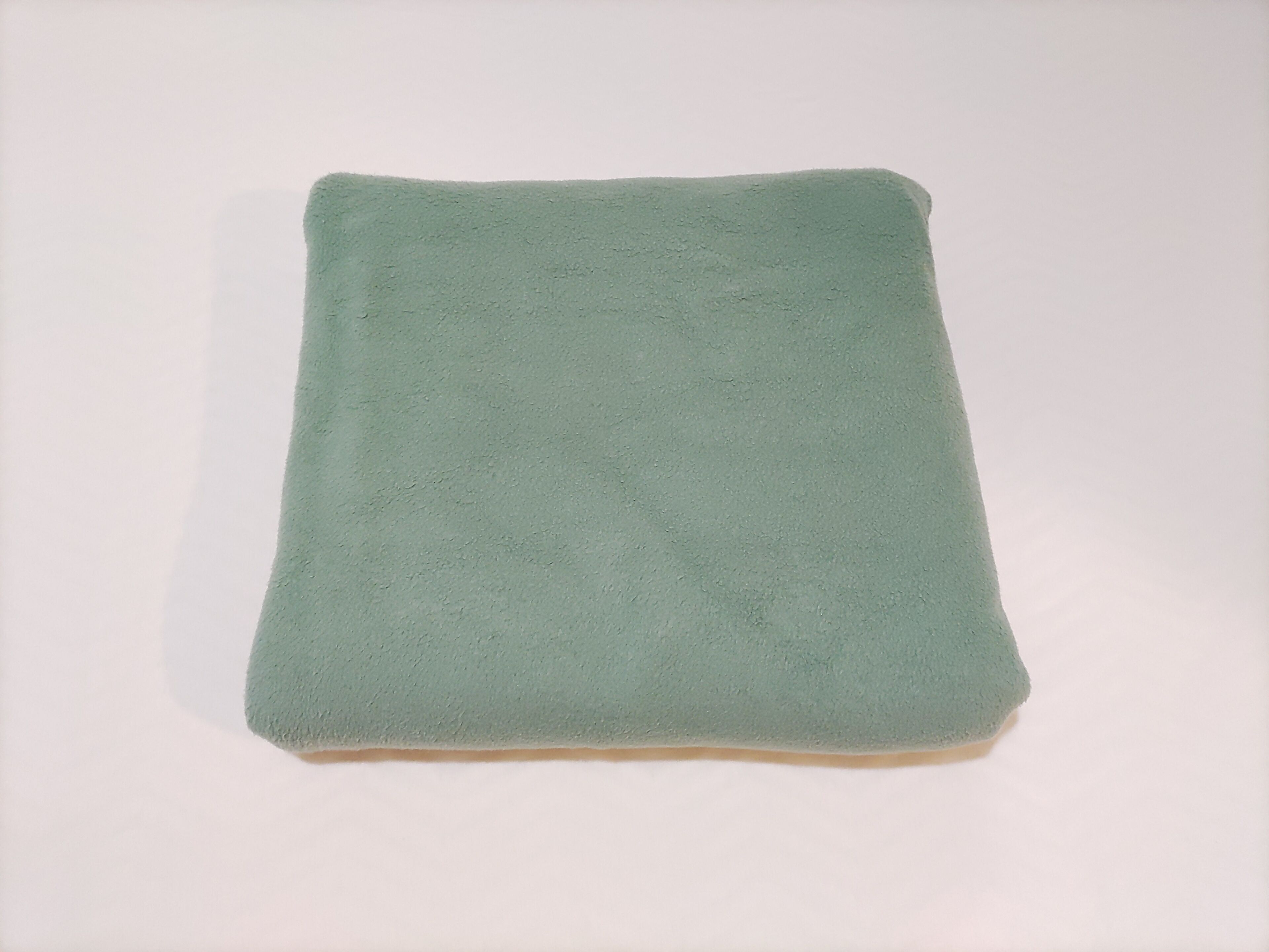 A folded green towel on a white surface.