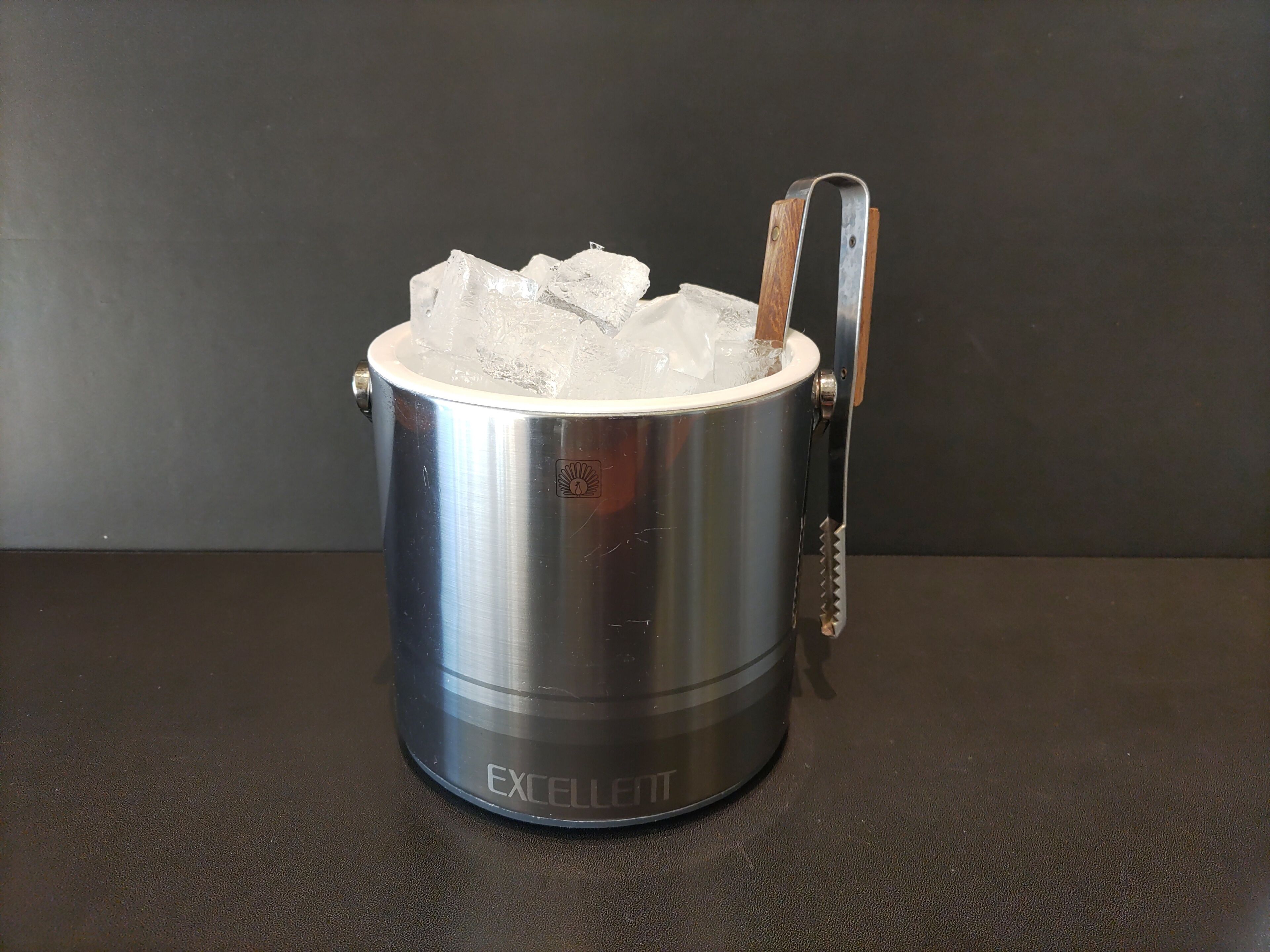 Un cubo de hielo de acero inoxidable con asa y caño, que contiene cubitos.