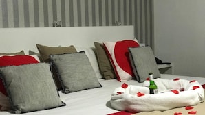A neatly made bed with a red and white blanket, multiple pillows, and a bottle of water on the side. - Hotel Argos Murcia (Cehegin)