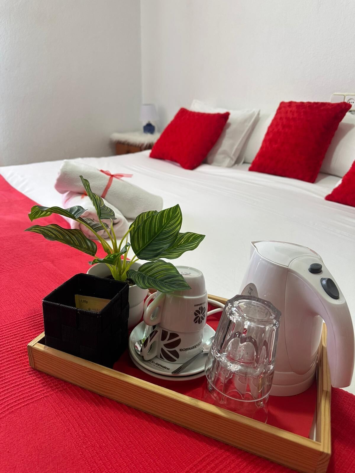 A hotel room with a bed, a tray with a plant, a coffee maker, and a glass.