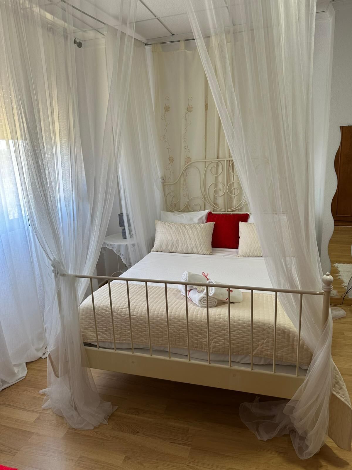 A bed with a white canopy, a red pillow, and a white pillow.