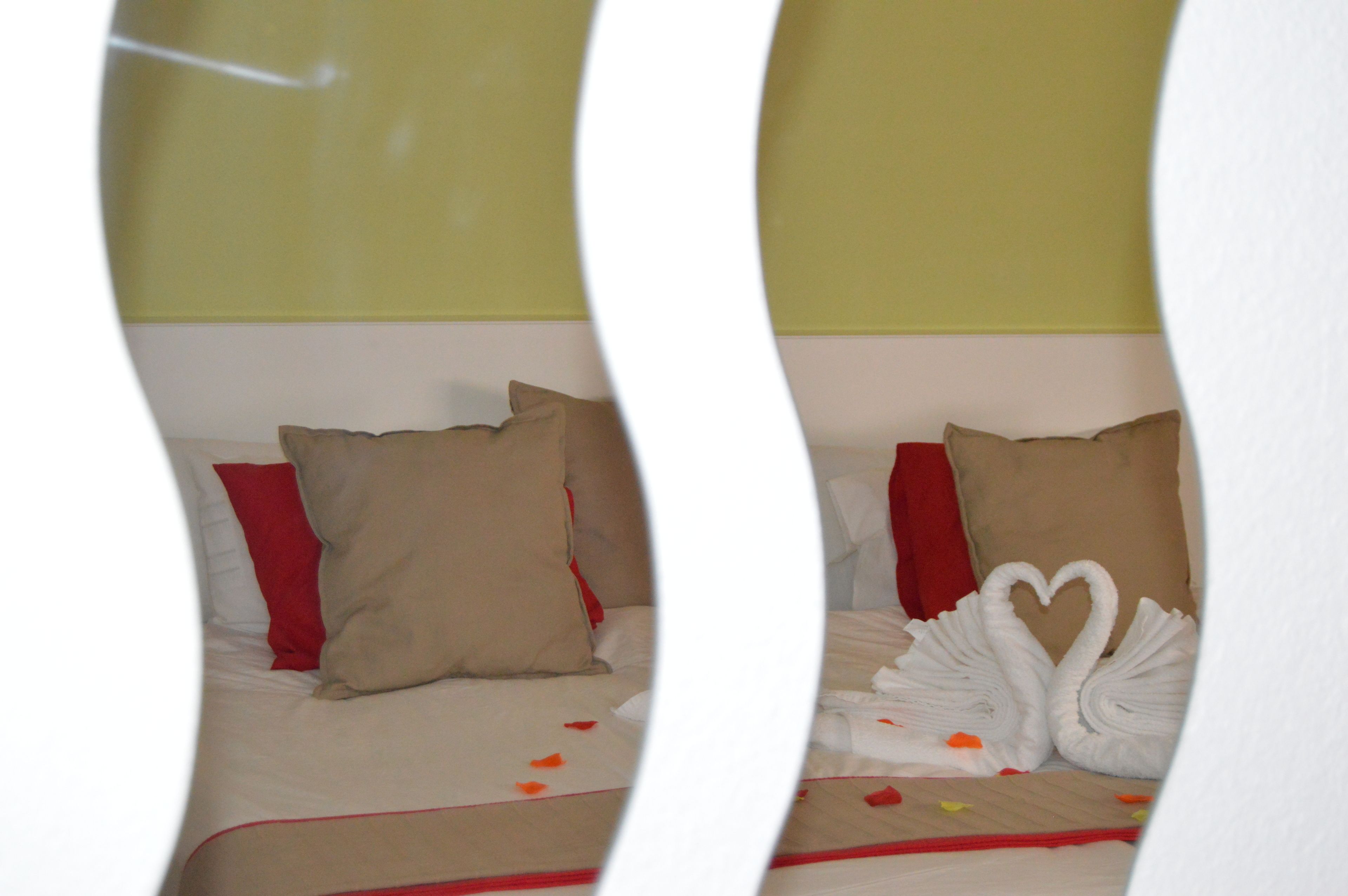 A hotel room with a bed featuring red and beige pillows, a white headboard, and a decorative swan towel arrangement.