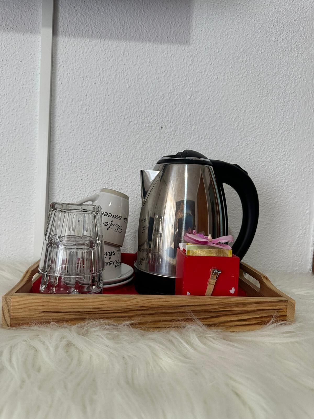 A tray with a stainless steel kettle, a glass pitcher, and a red box with a white lid.