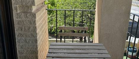 A balcony with a wooden bench and a table, overlooking a green landscape.