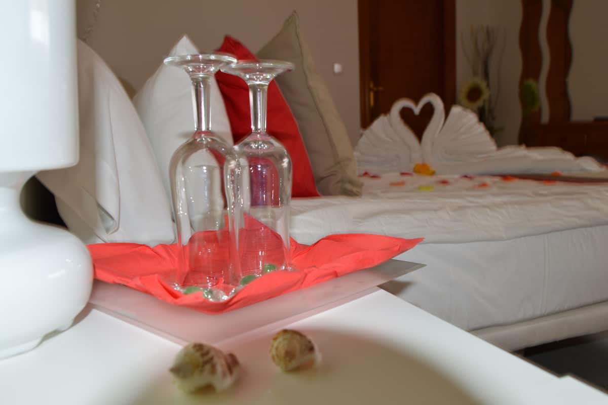 A neatly arranged hotel room with a bed, pillows, and a table with a red cloth and clear glasses.