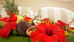 A tropical fruit and flower arrangement on a bed with a striped pillow.