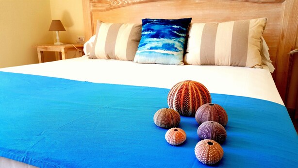 A bed with a blue bedspread, a wooden headboard, and a pillow with a blue ocean design.