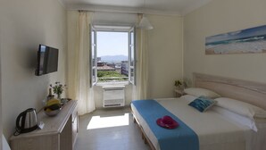 A hotel room with a bed, a television, a window with curtains, a painting, and a view of the city.