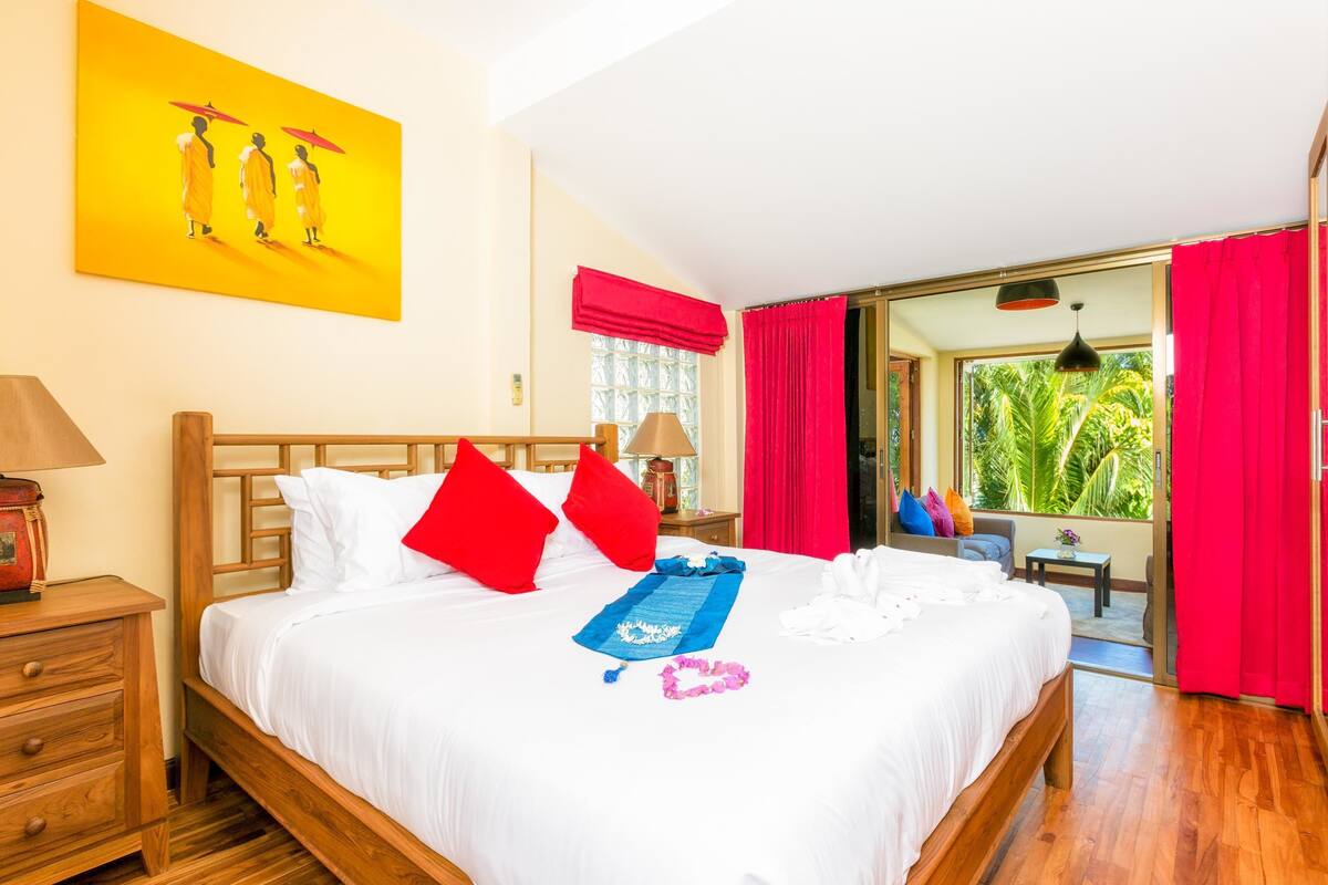 A hotel room with a wooden bed, red pillows, a blue towel, and a painting on the wall.