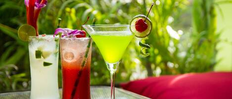 Three cocktails on a glass table with a red cushion in the background.