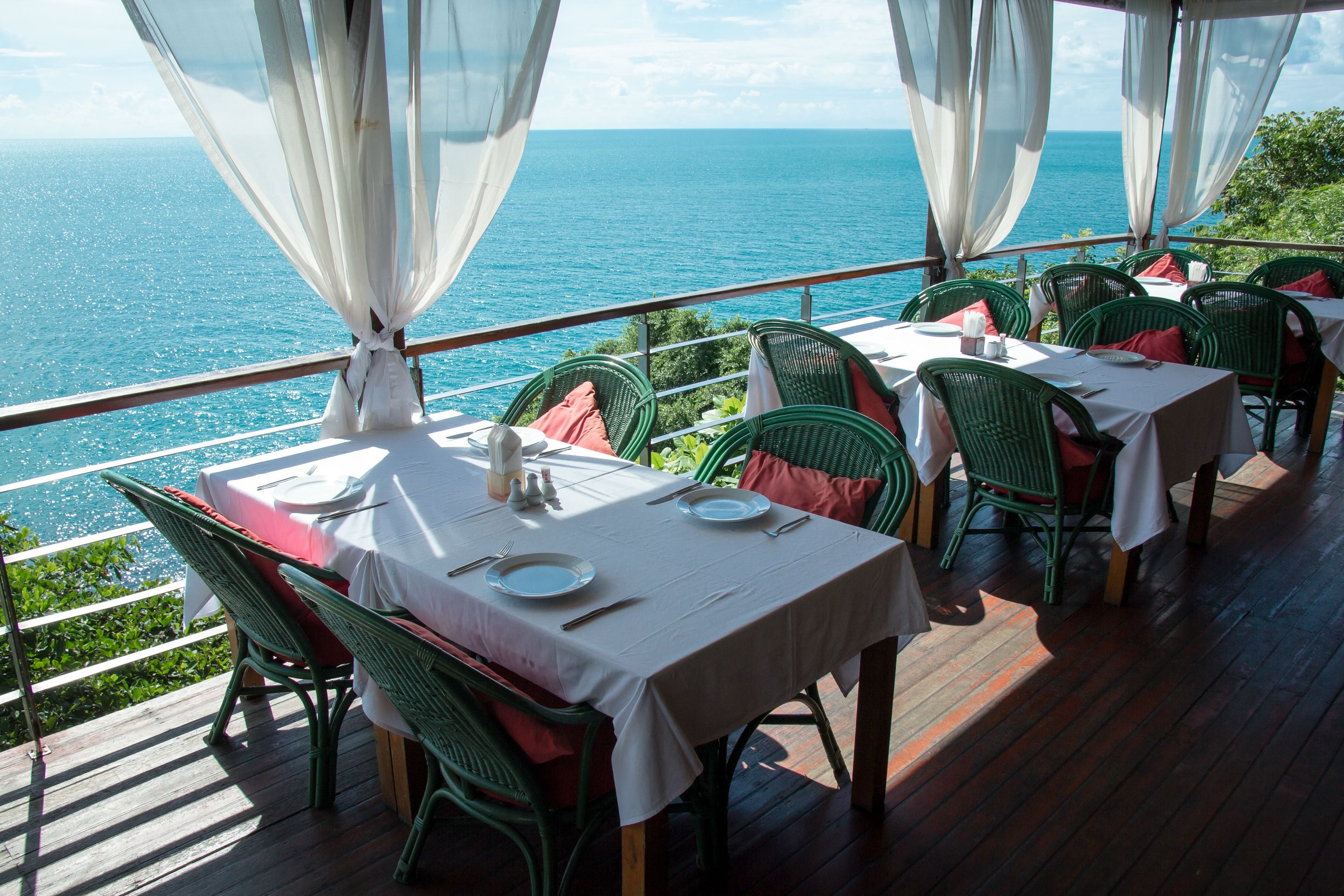 A dining area with tables set for two, overlooking the ocean.