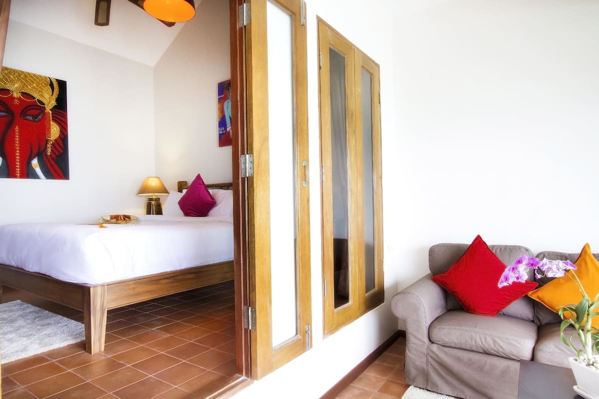 A bedroom with a bed, a sofa, and a window with wooden frames.