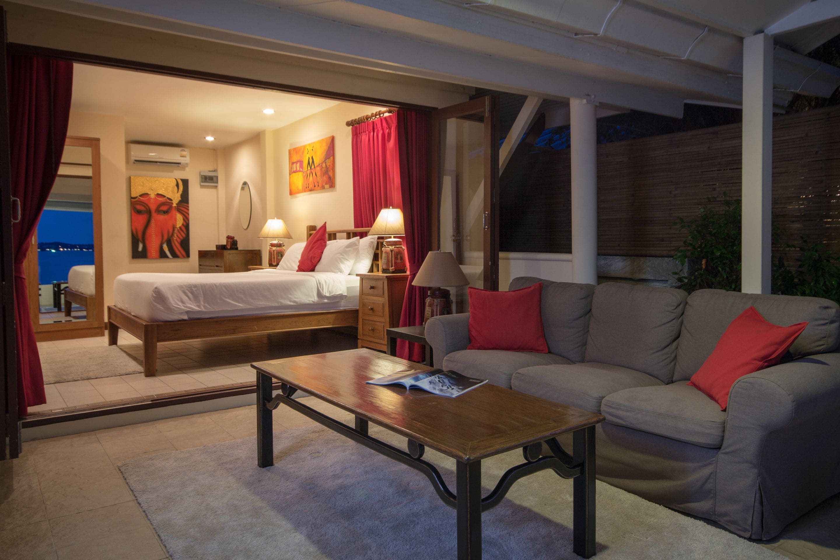 A hotel room with a bed, a sofa, a coffee table, and a view of the city at night.