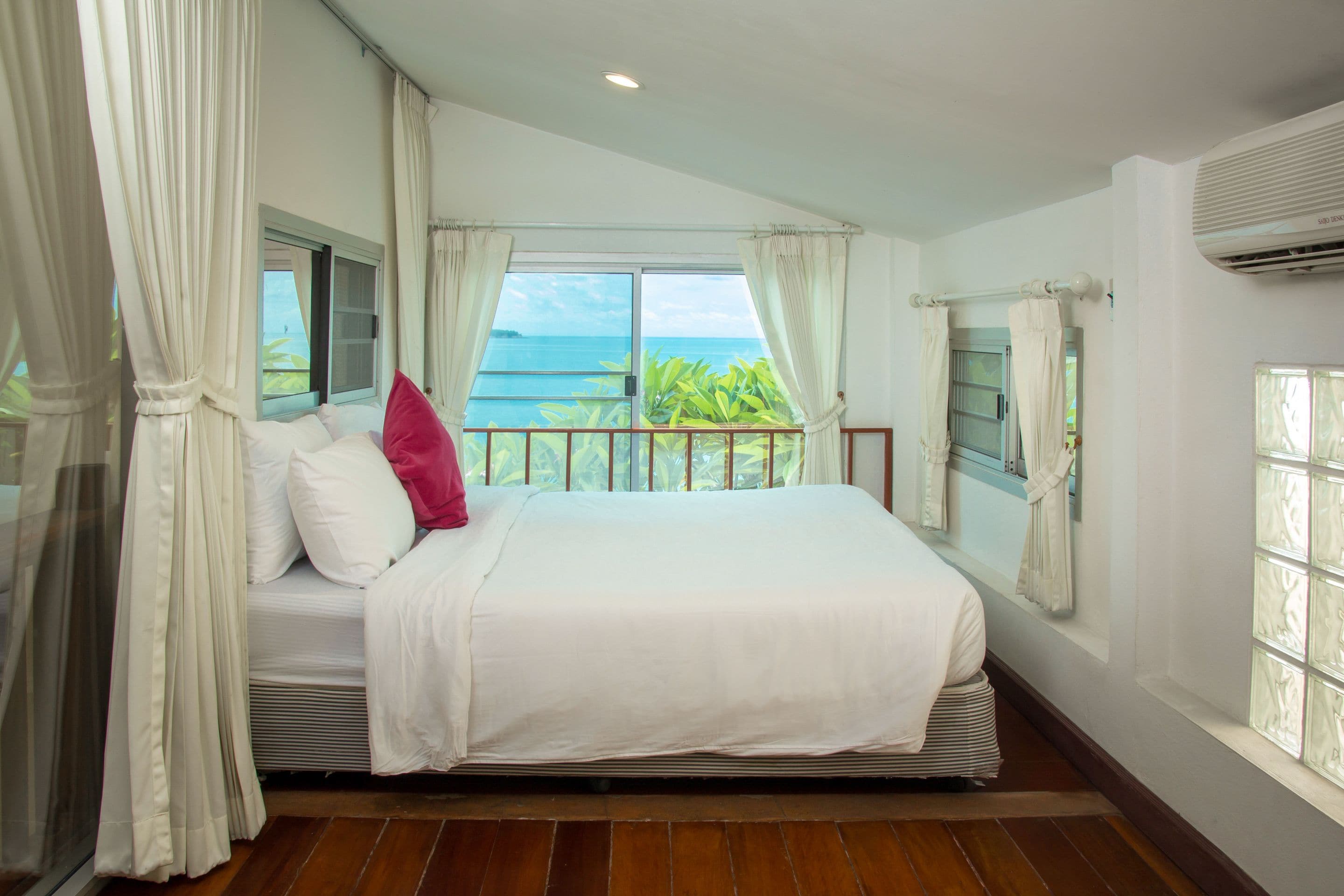 A bedroom with a large bed, white bedding, and a view of the ocean through a window.