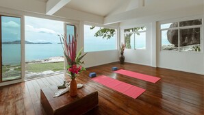 A spacious room with wooden flooring, large windows offering a view of the sea, and a wooden bench with a vase of flowers. - Boujis Boutique Resort (Koh Samui)