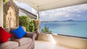 A covered balcony with a view of the sea, a stone sculpture, and a sofa with cushions. - Boujis Boutique Resort (Koh Samui)