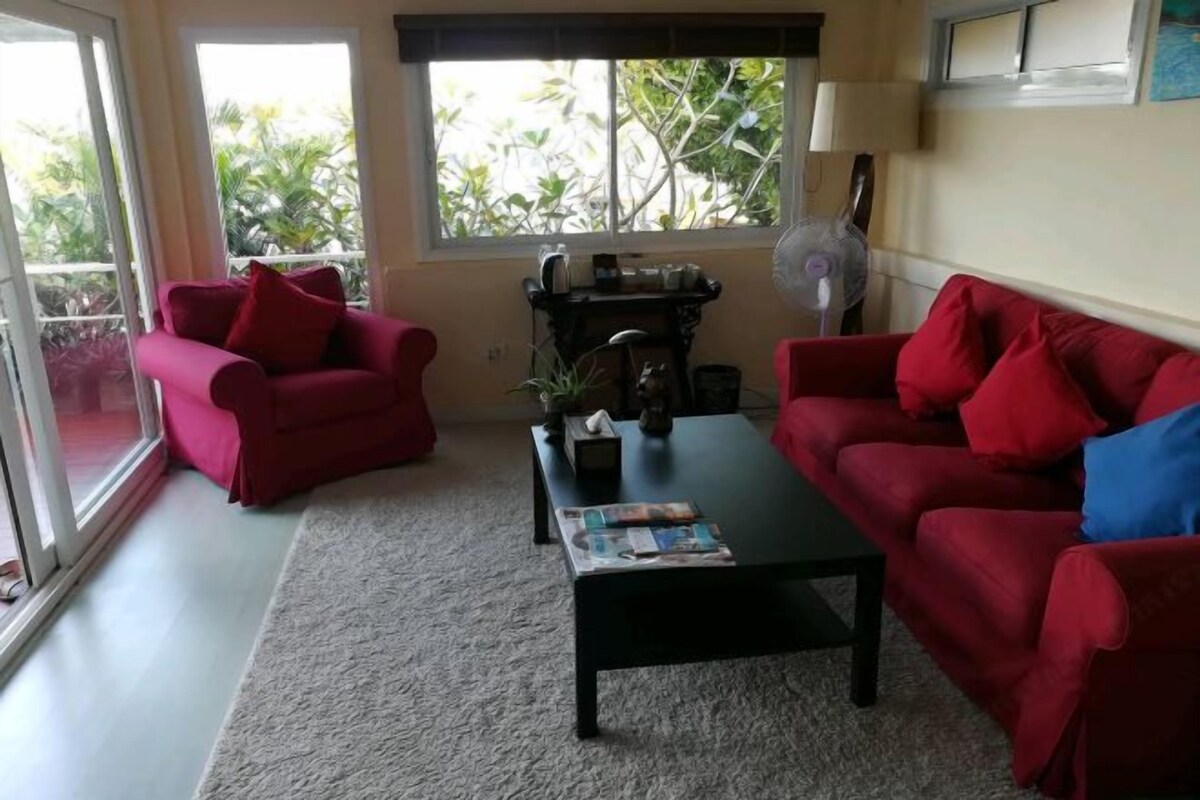 A living room with two red sofas, a black coffee table, and a window with a view of greenery.