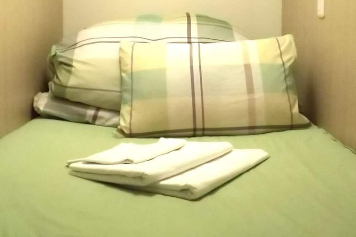 Ein Einzelbett mit einer grünen Bettdecke und zwei Kissen, eines kariert, das andere schlicht.