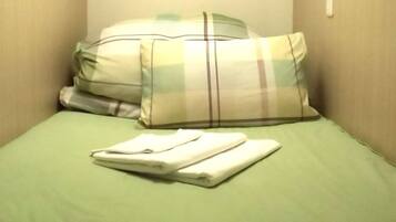 A single bed with a green sheet and two pillows, one with a plaid pattern and the other plain.