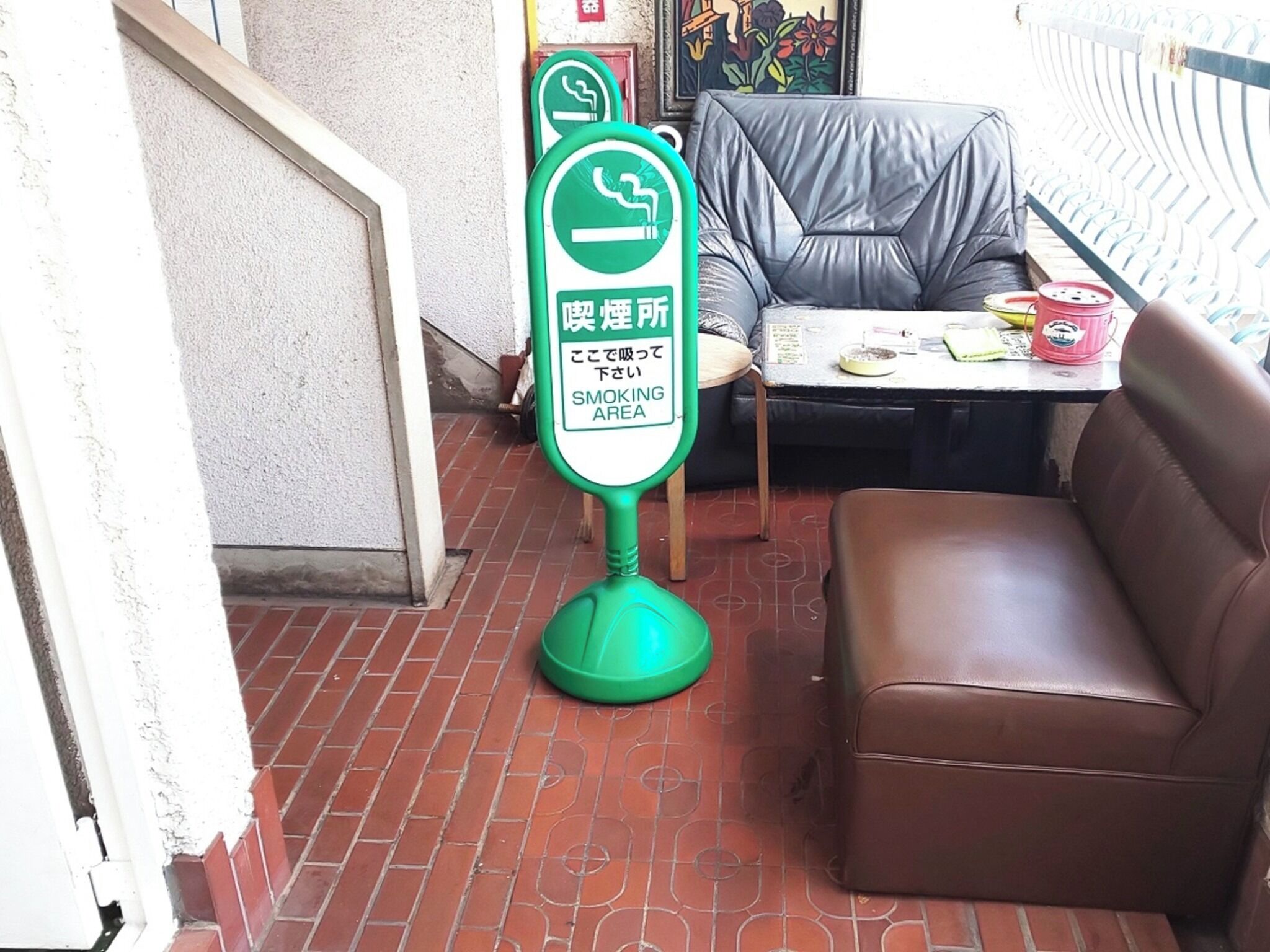 A smoking area sign, a brown leather couch, and a small table with items on it.