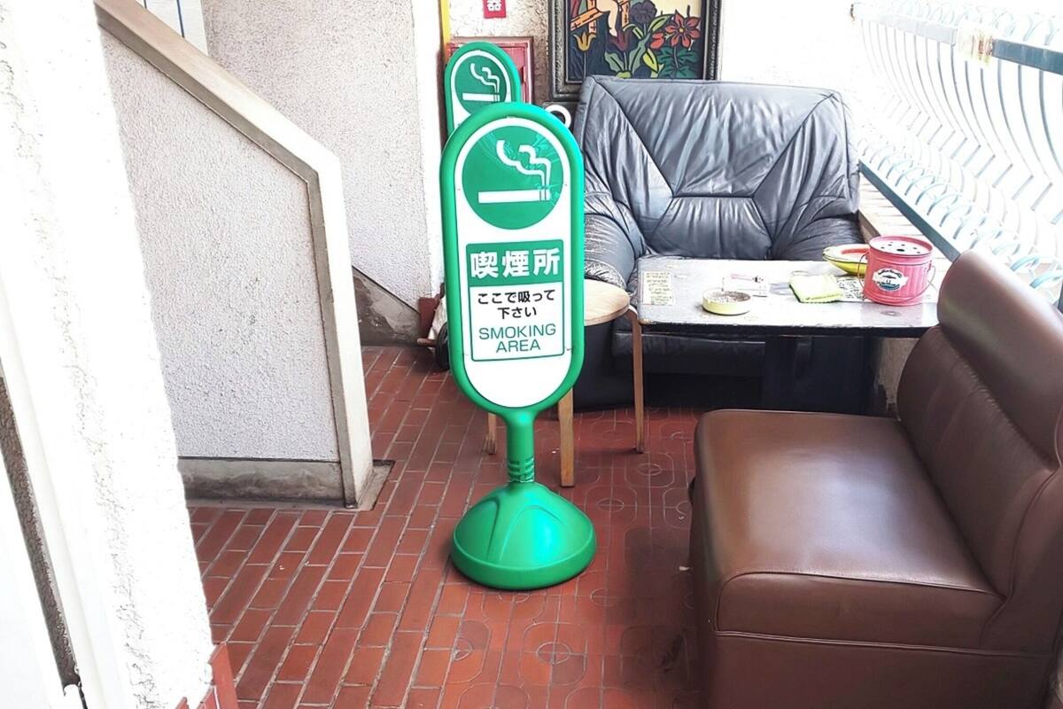 Ein Raucherecke-Schild, ein braunes Ledersofa und ein kleiner Tisch mit Gegenständen darauf.