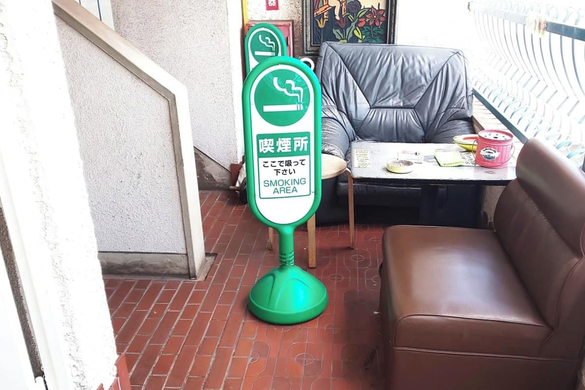 Ein Raucherecke-Schild, ein braunes Ledersofa und ein kleiner Tisch mit Gegenständen darauf.