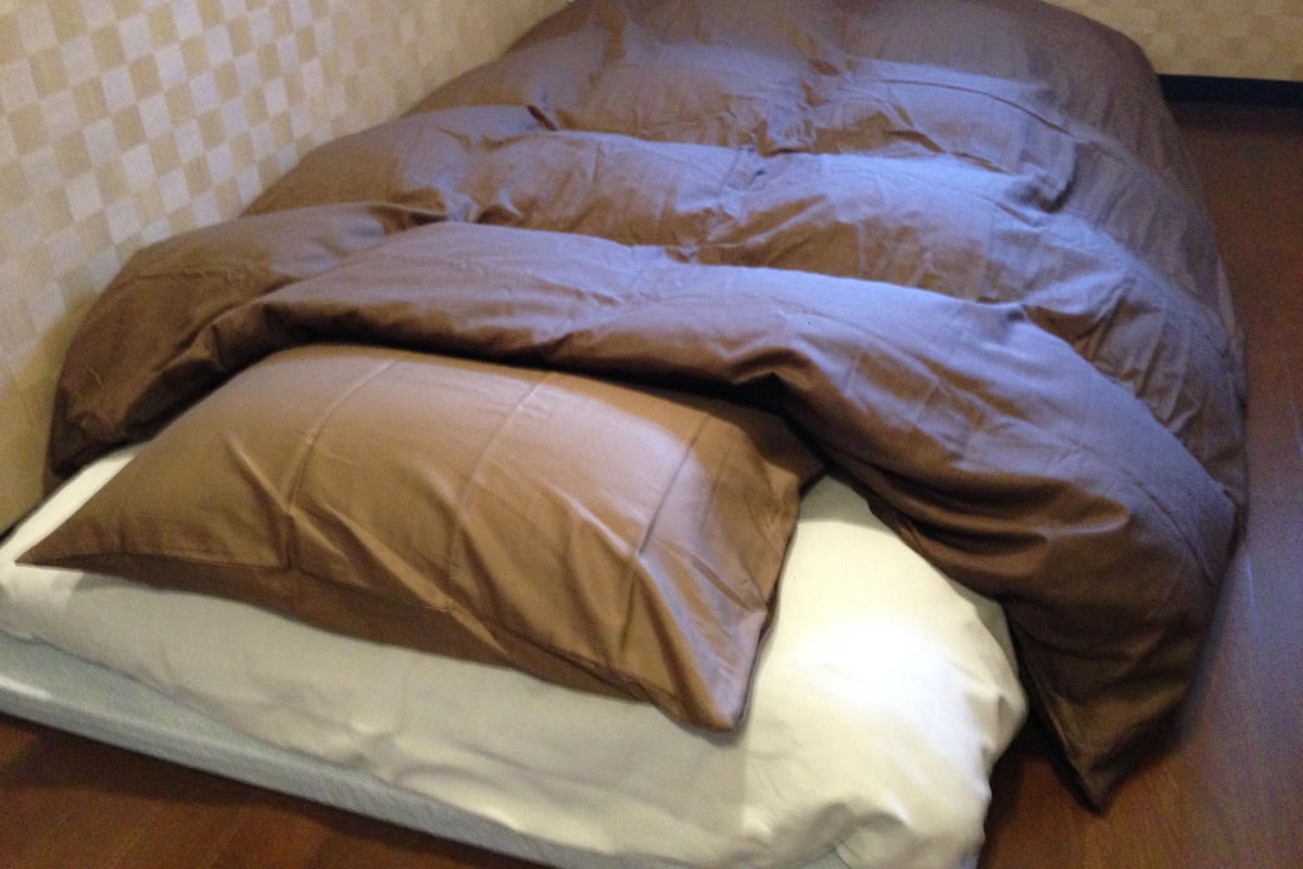 Ein Bett mit einer braunen Bettdecke und Kissen, einem weißen Matratze sowie einer Wand mit Muster im Hintergrund.