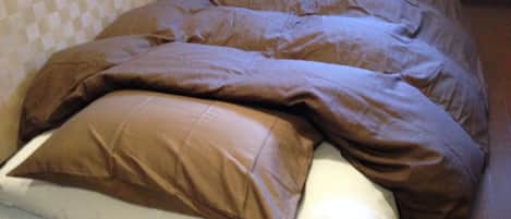 Una cama con una colcha marrón y almohadas, un colchón blanco, y una pared con un diseño en el fondo.