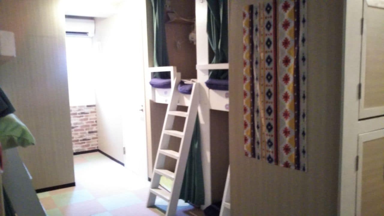 A room with bunk beds, a ladder, and a door with patterned curtains.