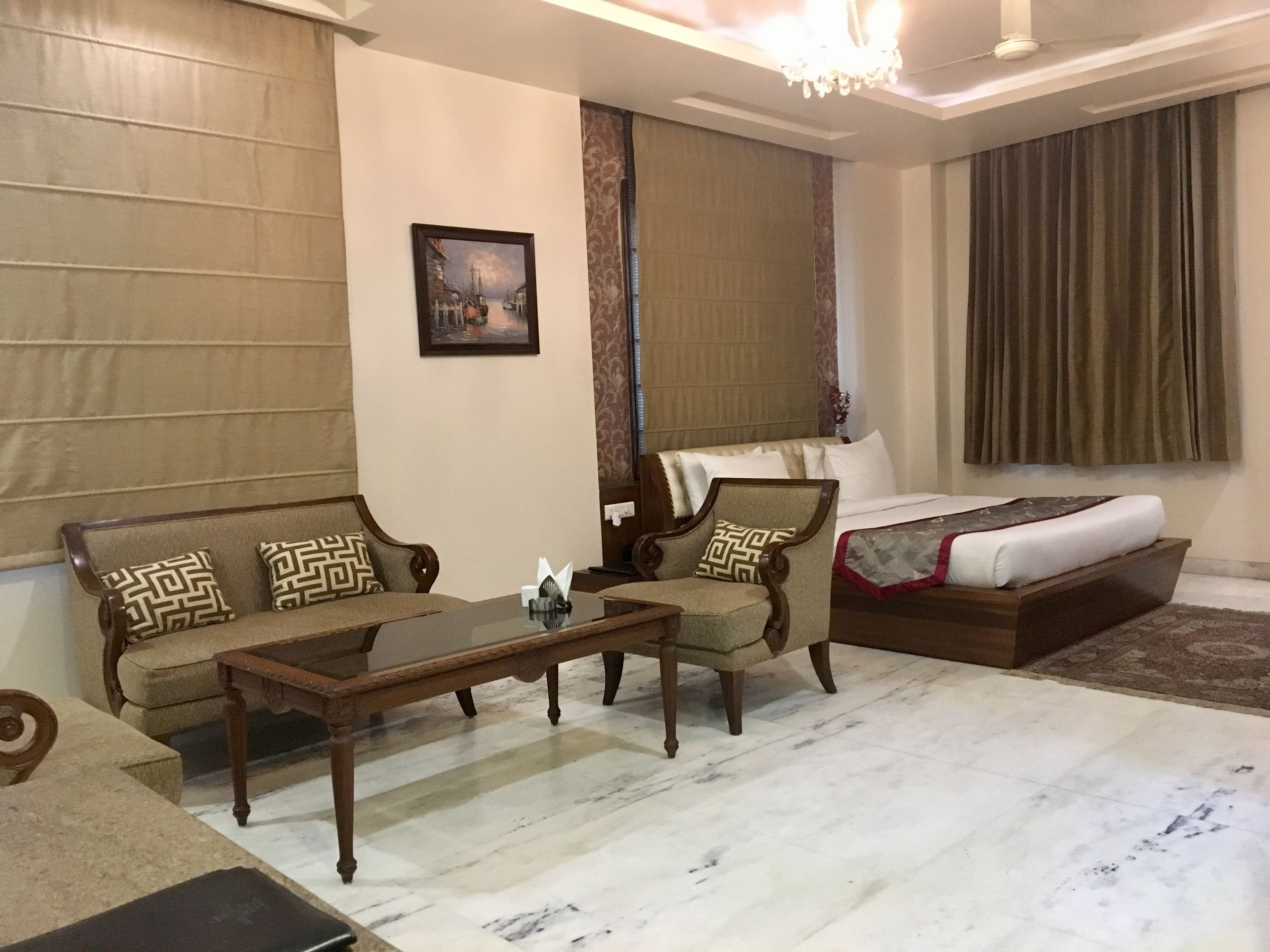 A hotel room with a sofa, armchair, coffee table, and a bed with a headboard.