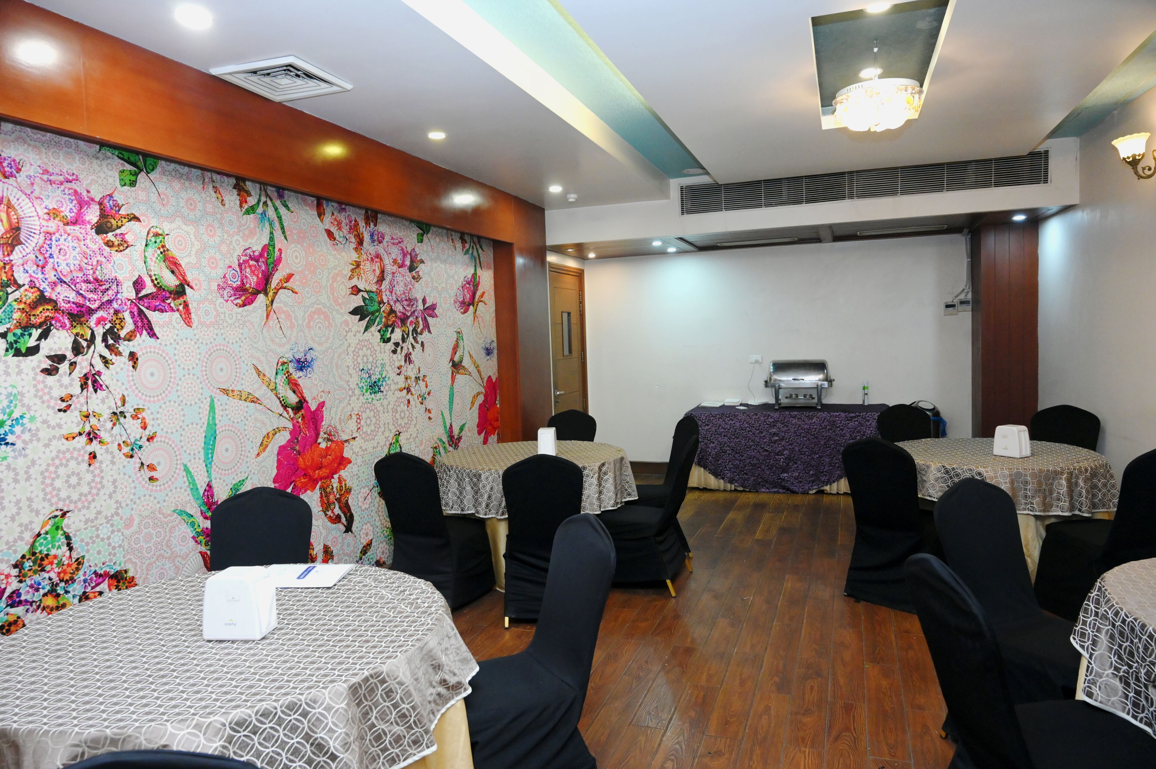A conference room with floral wallpaper, black chairs, and tables with lace tablecloths.