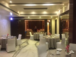 Comedor de hotel con mesas redondas, sillas blancas y suelo de mármol.
