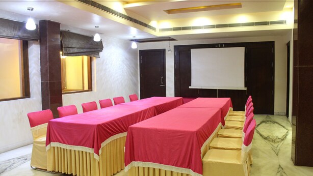 A conference room with long tables, chairs, a projector screen, and a large window. - Leela Grande Hotel (Karnal)